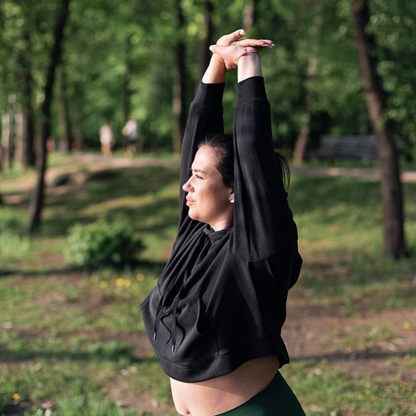 Smiling person stretching outdoors in a green park during a sunny morning.